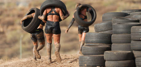 Mud race runners. Runners carrying tires in a test of the raceの写真素材
