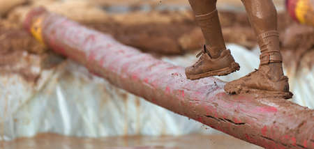 Mud race runners. Participant walking on the tree trunk, catches balance above the pit full of water