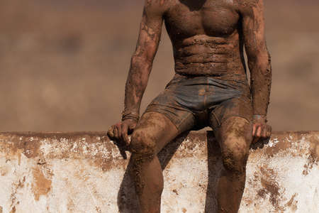 Mud race running. Running over obstacles male race participant, climbs over wall on obstacle courseの写真素材