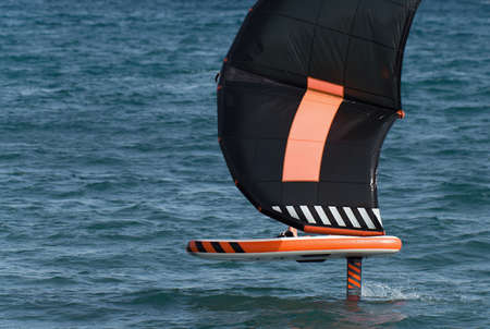 A man is wing foiling using handheld inflatable wings and hydrofoil surfboards in a blue ocean, rider on a wind wing board, surf the wavesの写真素材