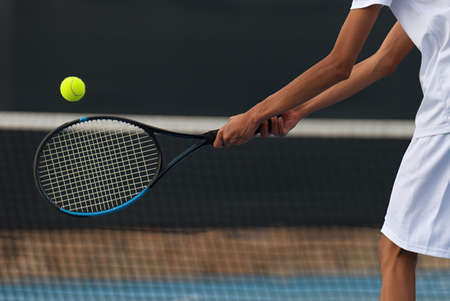 Male tennis player hitting backhand by net on the tennis courtの写真素材