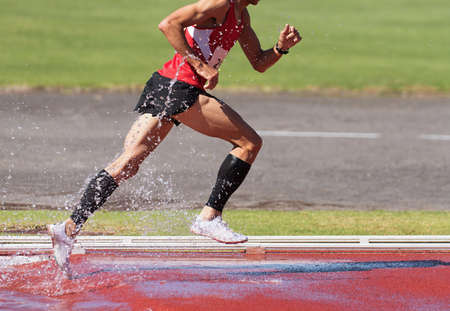 Runner running through the steeplechase water bake on a running track, steeplechase males athletes runner overcame water jumpの写真素材