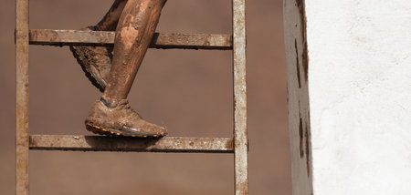 Mud race runner. The racer overcomes the obstacle by climbing the ladder