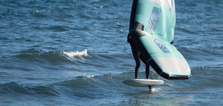 A man is wing foiling using handheld inflatable wings and hydrofoil surfboards in a blue ocean,...