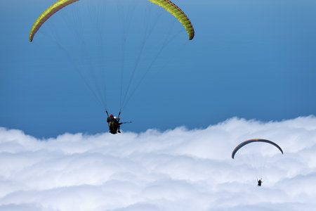 Flight above the clouds, paragliders are flying on a paraglider in the sky. Tandem flight above the...
