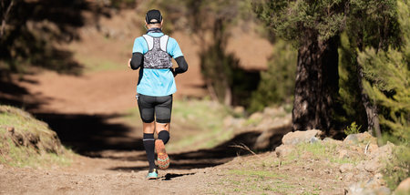 Athlete man running mountain marathon along a forest trail with a backpack