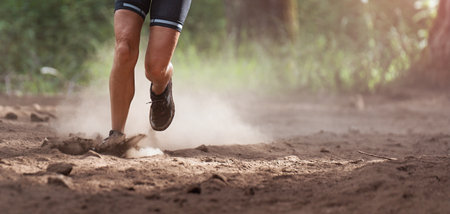 Trail runner running in summer mountain nature landscape on difficult path in mountains, running in a dusty environment in the forestの写真素材