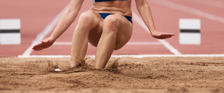 Female athlete long jump landing sand spray, landing in long jump in track and field