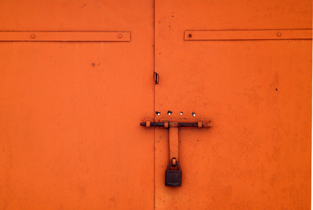 Orange color old padlock on metal gate. Abstract background and texture.の写真素材