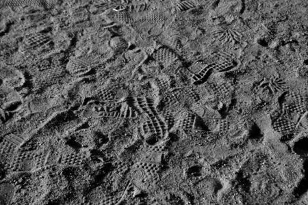 Many footprints in the sand in black and white. Abstract background and surface for design.
