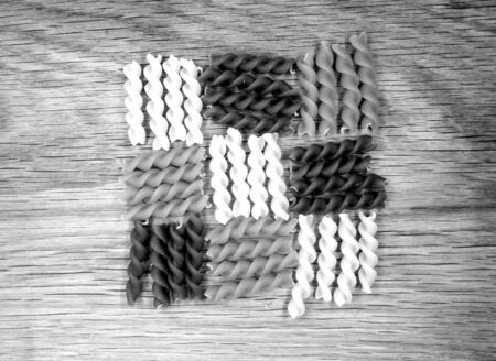Dry multi-colored pasta on wooden board in black and white. Food and ingredientes background.