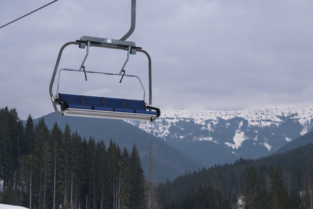empty four seats ski snowboard chairlift lift at ski resort with beautiful mountains and forest landscape with cloudy sky on the backgroundの写真素材