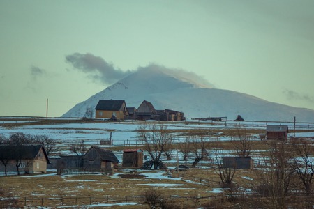 landscape picturesque view of a little village with few little wooden houses at the hills with snowy mountain at the backgroundの写真素材