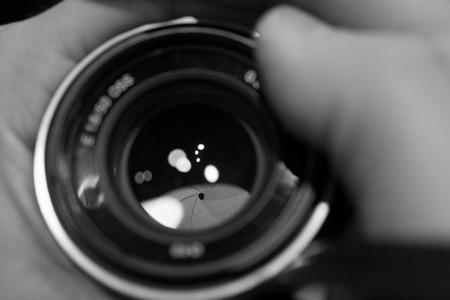 closeup macro of camera lense in hands with reflections low key black and white image with aperture bladesの写真素材