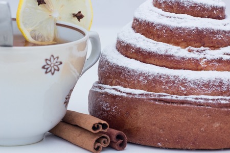closeup shot of cinnabon covered with sugar powder croissant roll with cinnamon and tea cup with lemonの写真素材