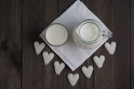 jug and glass with milk and heart cookies on white tissue napkin and wooden backgroundの写真素材