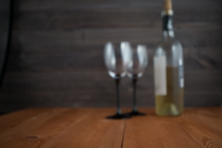 blurred image with two wine glasses and bottle of white wine. wooden background. selective focus. out of focus imageの写真素材