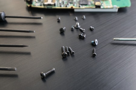 closeup shot of a a black screws and disassembled smartphone with screwdrivers. focus on screwsの写真素材
