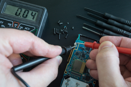 pov shot of technician hands measure voltage, amperage on broken smartphone by multimeter with probes. on black deskの写真素材