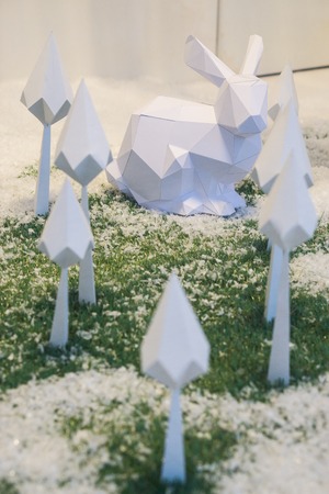 Christmas winter origami. white rabbit and white paper trees on green grass covered with snowの写真素材