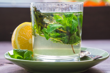 a cup of fresh mint tea on a dark wooden table with leaves of fresh mint and lemon. side view at...
