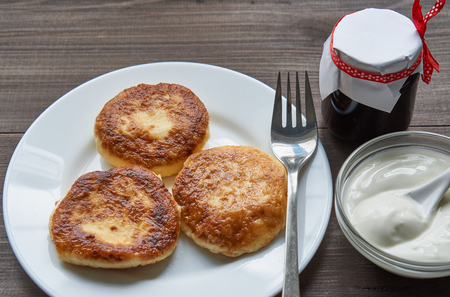 three pancakes on a white plate with sour cream on a dark table and small jar with jam. low angle view.の写真素材