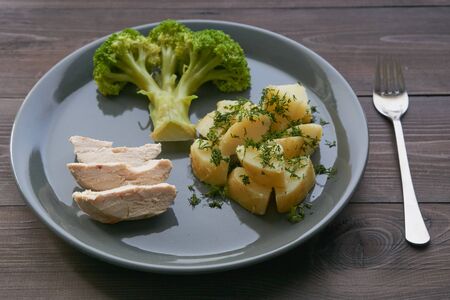 healthy useful lunch boiled broccoli potato and chicken on a gray plate on a dark brown wooden tableの写真素材