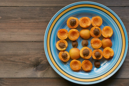 pattern mosaic apricots on a blue plate on a wooden table. apricots cut in a half. top viewの写真素材