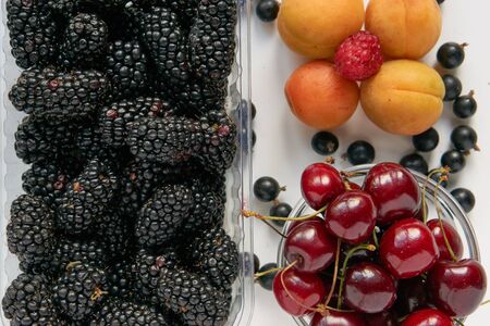 fresh tasty blackberry, cherry and apricots in a plastic transparent tray bowl isolated on white background cutout. top view from aboveの写真素材
