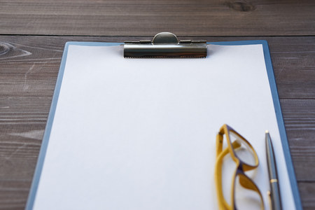 empty paper on a desk with glasses and pen on a side. low angle view