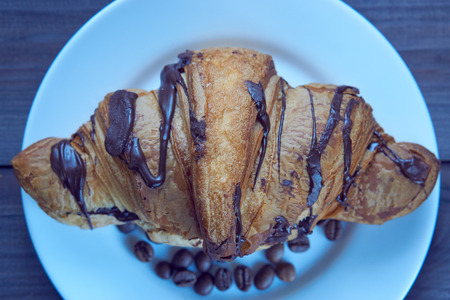 closeup crispy homemade croissant decorated with chocolate icing on a white plate with coffee beans. from the topの写真素材