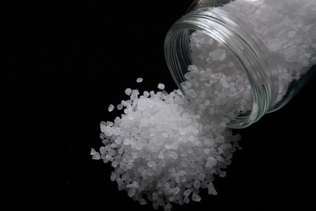 closeup of a small sea salt crystals pile spilled from small jar isolated on black background. low...