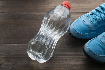 water bottle and light blue pair of running shoes sneakers on dark wooden background. flat top angle viewの写真素材