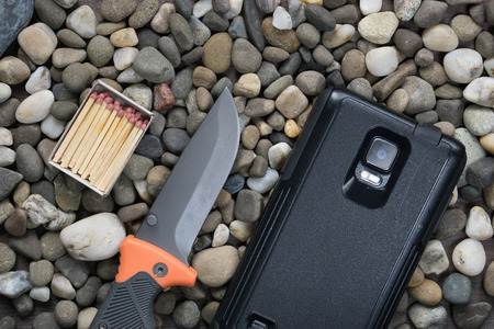 nowadays modern survival kit. box with matches, folding knife and rugged tough smartphone on rocks....