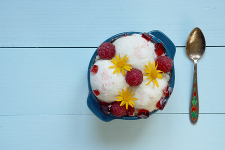 top view on ice cream in a bowl. with raspberries, yellow flowers an syrup on top. cute small spoon for delicious dessert on the right. aerial viewの写真素材