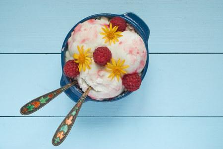 top view on ice cream in a blue ceramic bowl. with raspberries, yellow flowers an syrup on top and two cute small spoons for couple. low angle portrait vertical shotの写真素材