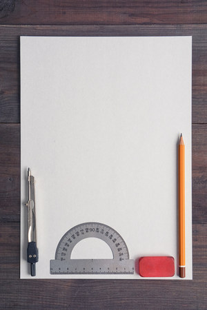 empty cardboard one single sheet of white paper letter on dark wooden desk with pencil, vivid red eraser, protractor and compass. aerial flat lay top view. simple for copy space needsの写真素材