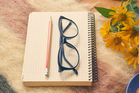 paper notebook with pen and glasses on woolen plaid with yellow flowers aside. cozy relax home environment to calm and make some notes. closeup low angle shotの写真素材