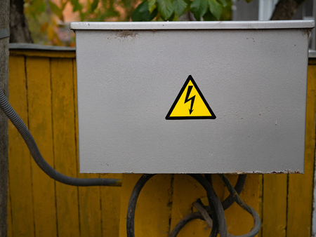 close up of closed gray electrical junction box with caution warning danger sign thunder in yellow...