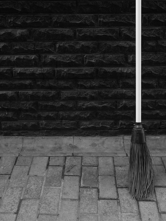 black and white photo of the broom at tile pavement near black wall. minimalistic cleaning business concept outdoor shot. improvement of public servicesの写真素材