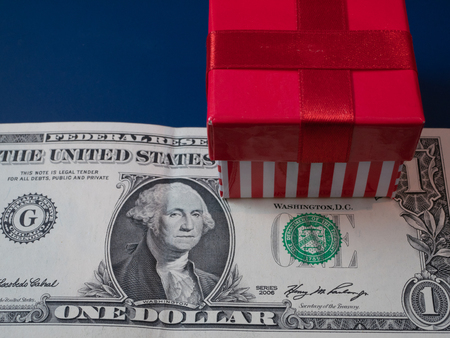 small gift box with red stripes ribbons on one dollar bill. closeup shot. cheap inexpensive present conceptの写真素材