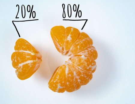 small and big slices of vivid yellow pilled mandarine. depict sales of exotic fruit market pareto rule concept. market share 20 and 80 percent signsの写真素材
