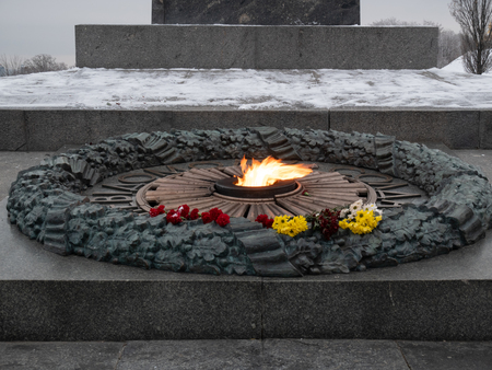 fresh flowers at eternal quenchless flame at the monument of World War II in Kyiv, Ukraine. in memory for all soldiers who fall in fight for freedom. outdoor winter twilight sunset evening shotの写真素材