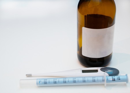 bottle with anti flu potion empty label, electrical thermometer and syringe for baby care portional dose dispenser. close-up on white background and lot of copy spaceの写真素材