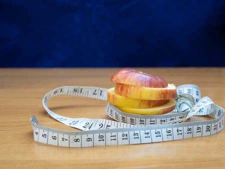 sliced apple among ruler on wooden desk. fitness lost weight concept. front shot with blue backgroundの写真素材