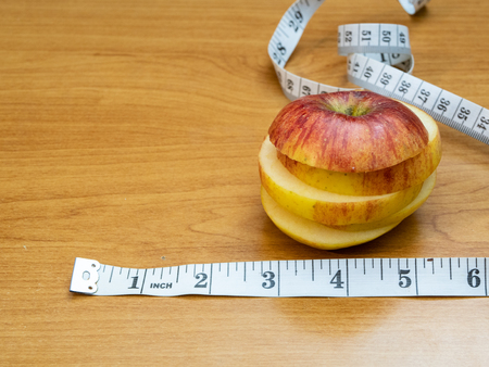 sliced apple by measuring tape with inches on wooden table, fruit diet conceptの写真素材