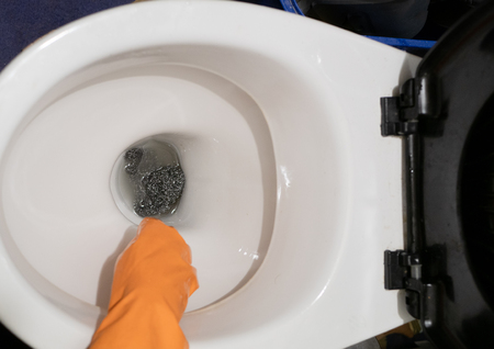 hand in orange glove clean toilet seat with metallic scrub. from the top. cleaning company service...