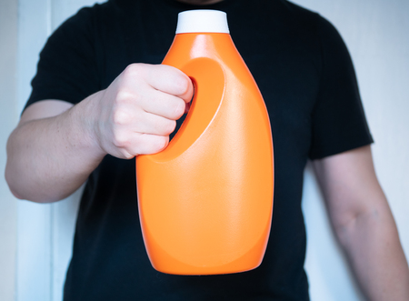 closeup orange color plastic bottle of detergent or washing machine gel in mans hand. housekeeping household conceptの写真素材