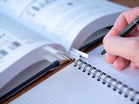 selective focus image of witer or student hand with pen above blank page of binder textbook. blurred opened book on backgroundの写真素材