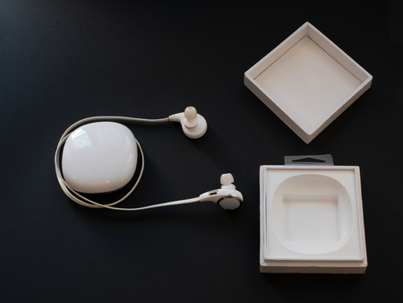 white opened box with wireless in-ear headphones headset on black background. low key imageの写真素材